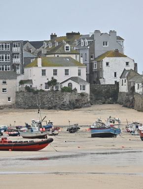 Afbeelding van een strand met daarop vissersboten en op de achtergrond woningen.