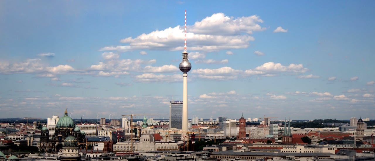 Afbeeling van de tv-toren in Berlijn in Duitsland met een blauwe lucht en stapelwolken op de achtergrond.