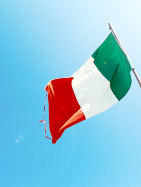 Afbeelding van een vlaggenstok met italiaanse vlag met een blauwe lucht als achtergrond en een felle zon.