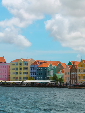 Afbeelding met op de voorgrond een zee, waaraan woningen staan die in vrolijke kleuren zijn geverfd.