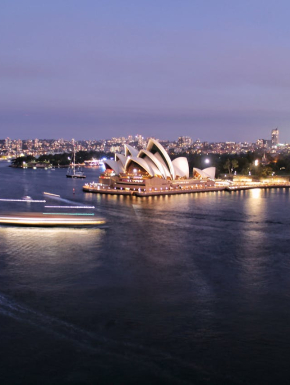Afbeelding van het Opera House in Sydney met schemer. Op de voorgrond is de zee.