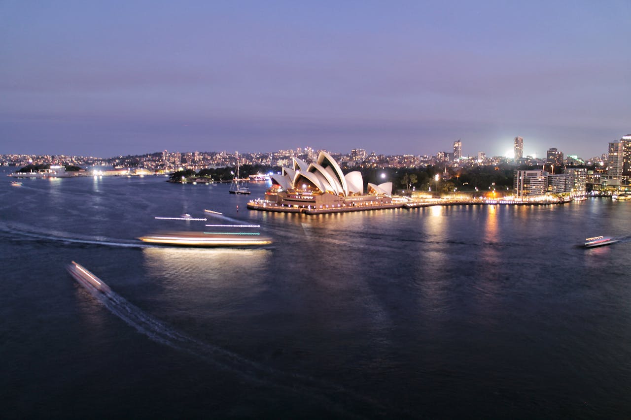 Afbeelding van het Opera House in Sydney met schemer. Op de voorgrond is de zee.